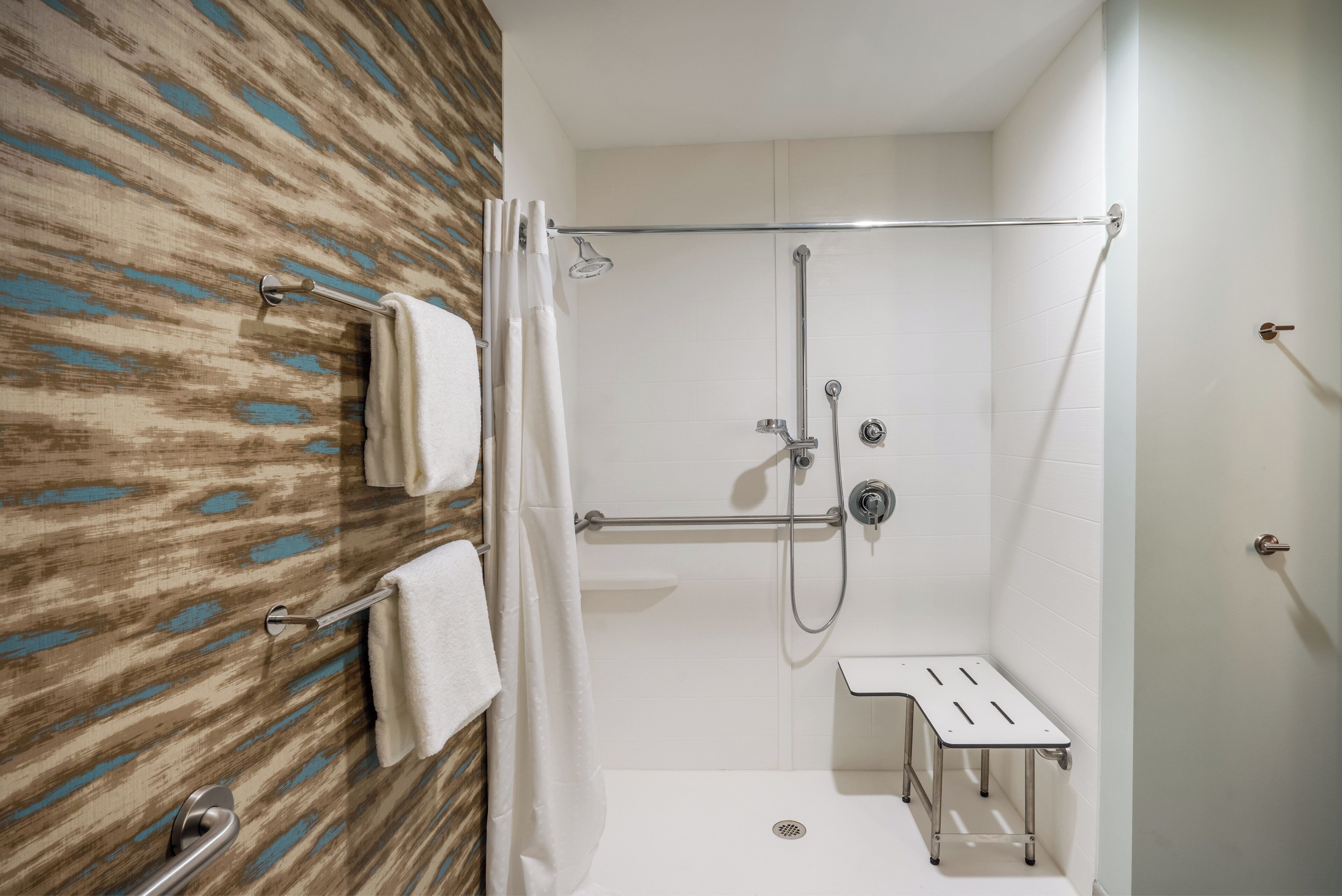 A shower area with a glass door, a towel rack with towels, and a small bench.