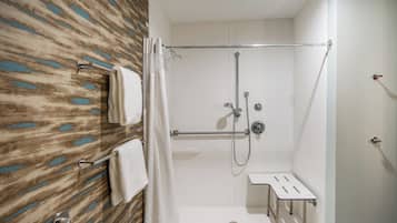 A shower area with a glass door, a towel rack with towels, and a small bench.
