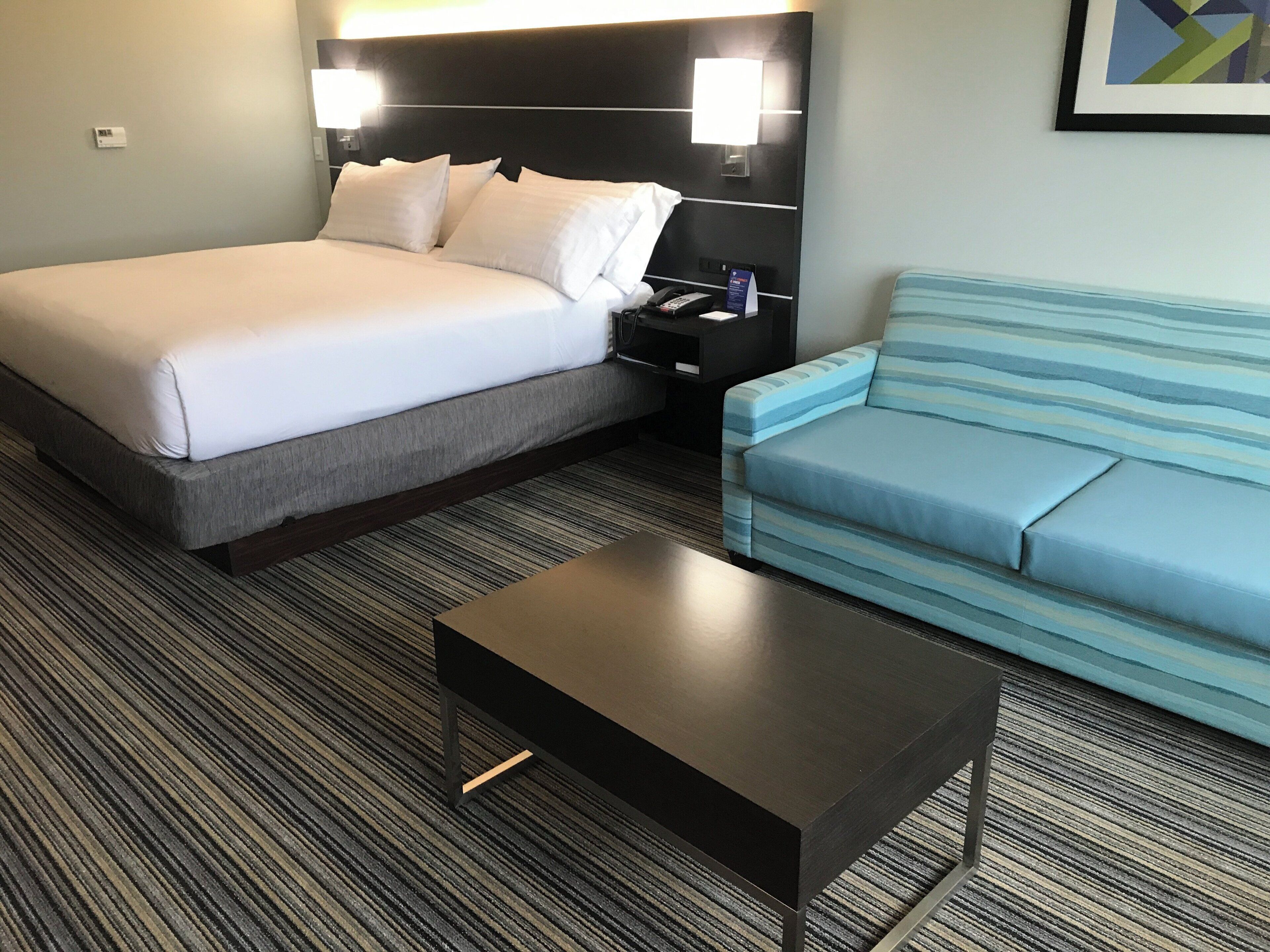A hotel room with a bed, a nightstand, a lamp, a sofa, and a coffee table.