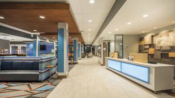 A hotel lobby with a reception desk, seating areas, and a corridor leading to other rooms.