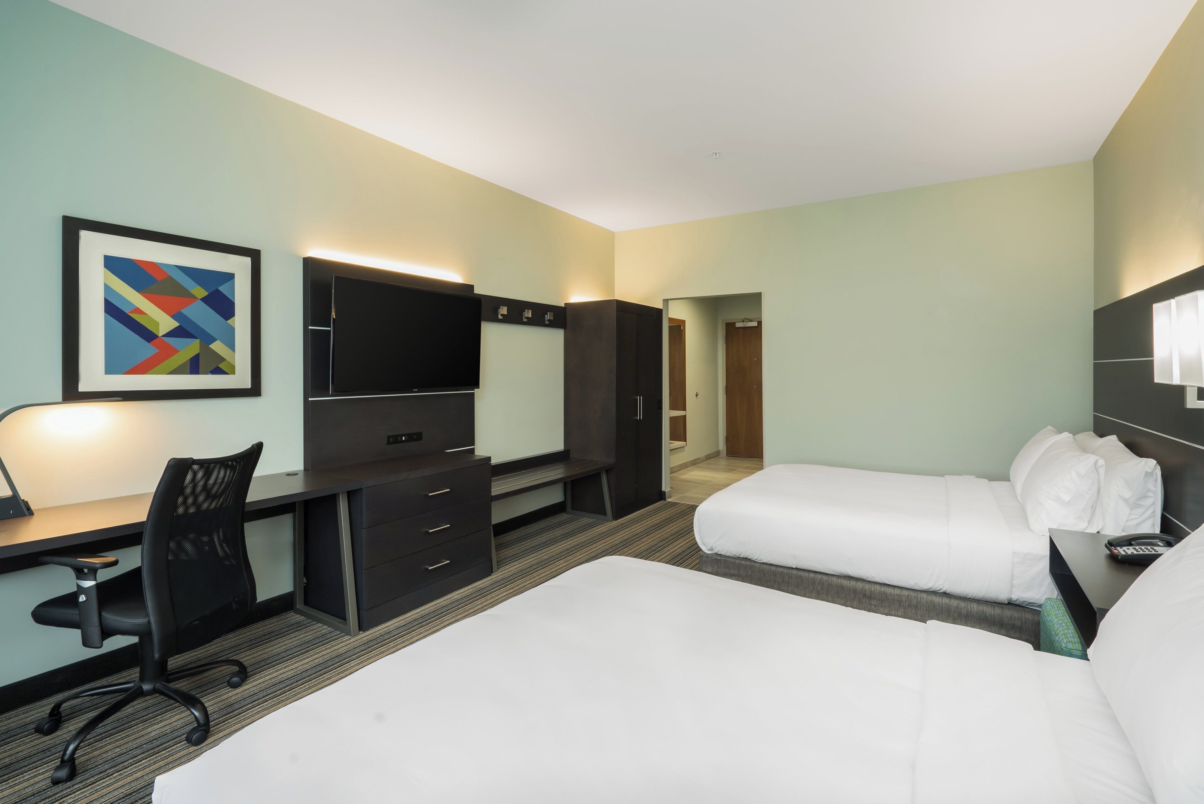 Ein Hotelzimmer mit Schreibtisch, zwei Betten, Fernseher und einem gerahmten Bild an der Wand.