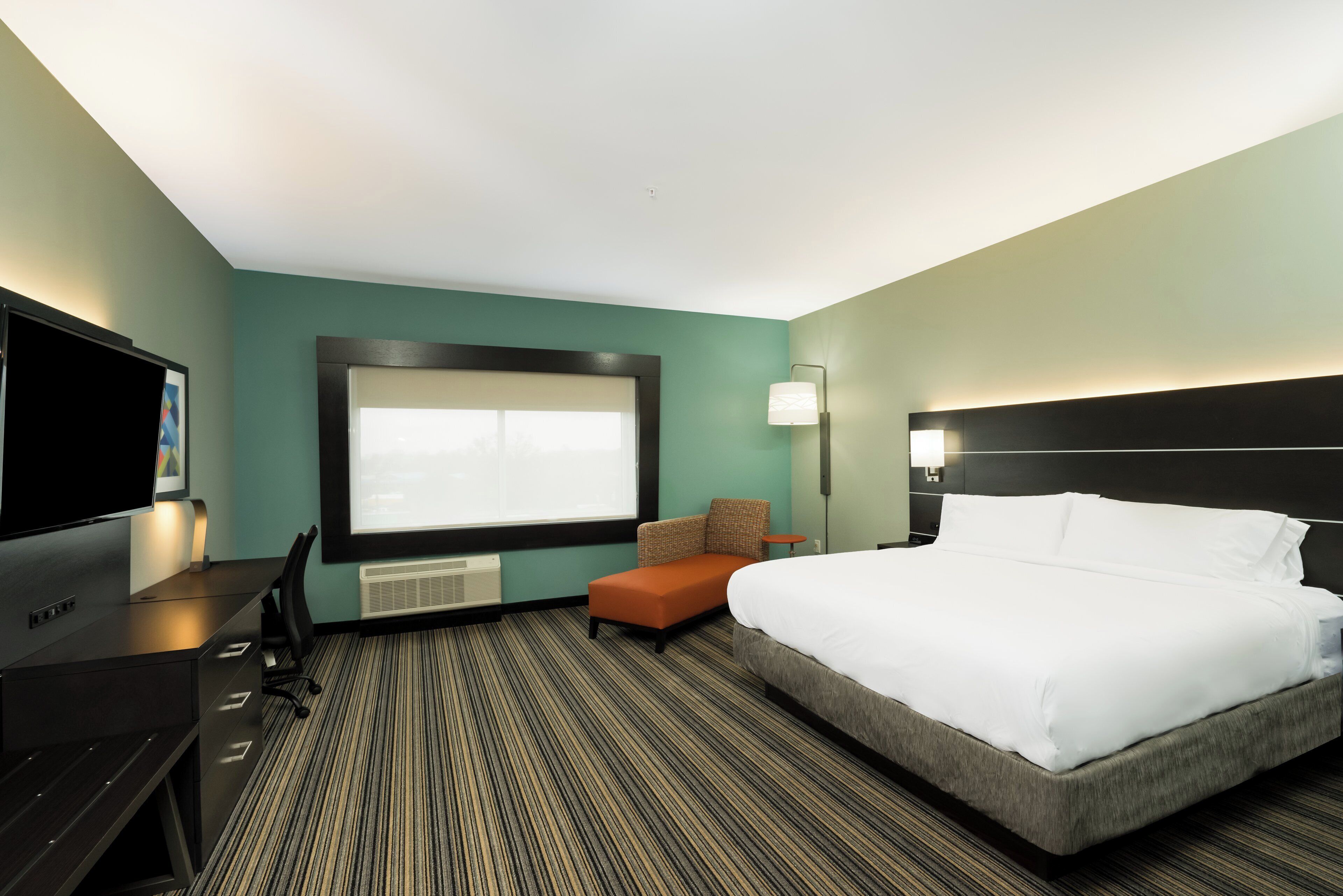 Habitación de hotel con una cama grande, un escritorio con televisor de pantalla plana, una silla y una mesita.