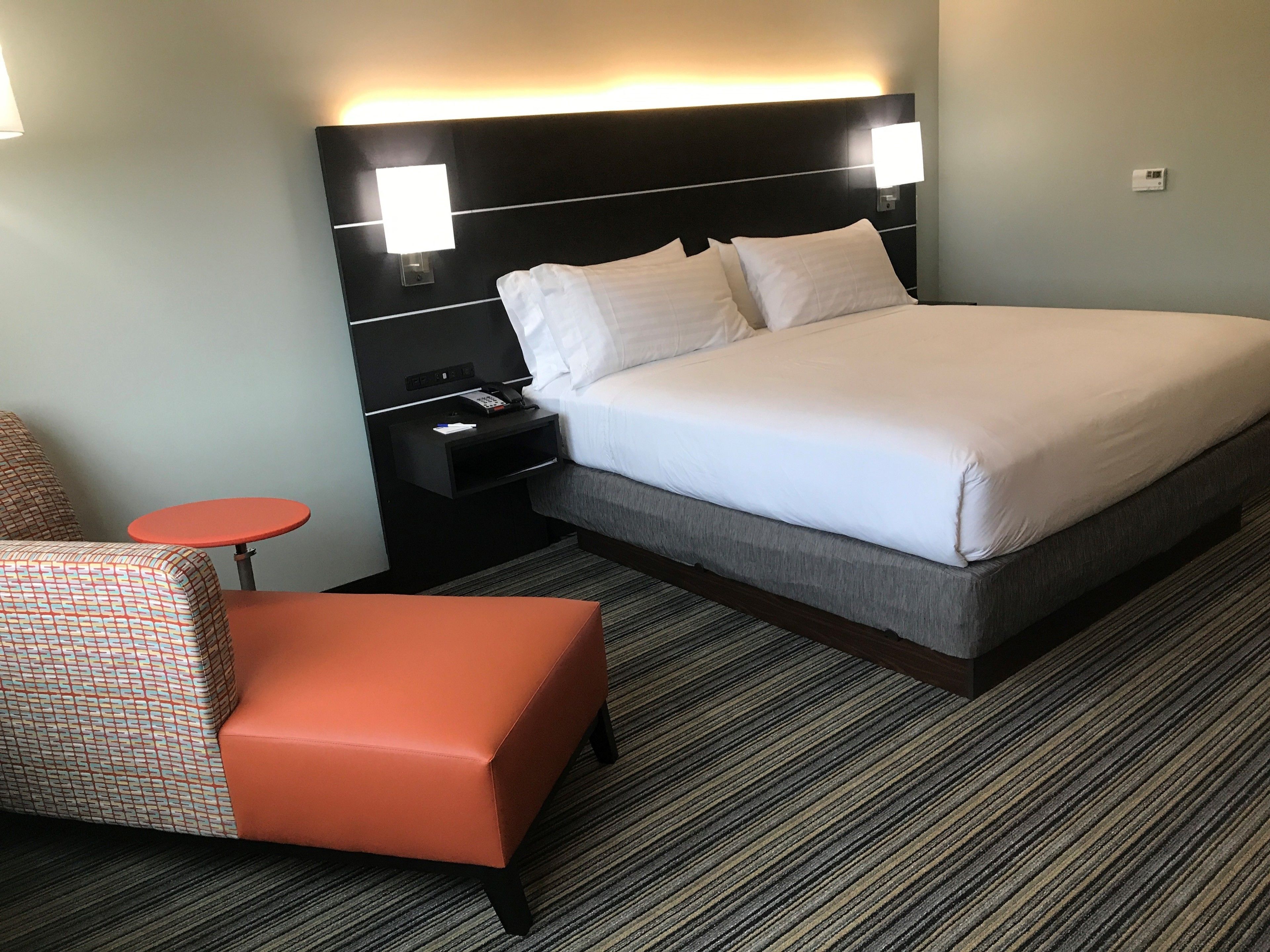 A hotel room with a large bed, a nightstand with a phone, a small table, and a chair.