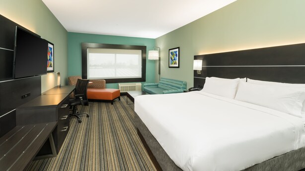 Une chambre d’hôtel avec un grand lit, un bureau avec une chaise, une télévision et une fenêtre avec des stores.