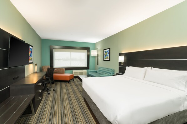 Ein Hotelzimmer mit einem großen Bett, einem Schreibtisch mit Stuhl, einem Fernseher und einem Fenster mit Jalousien.