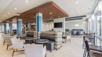 A modern lounge area with seating, tables, and a TV screen.