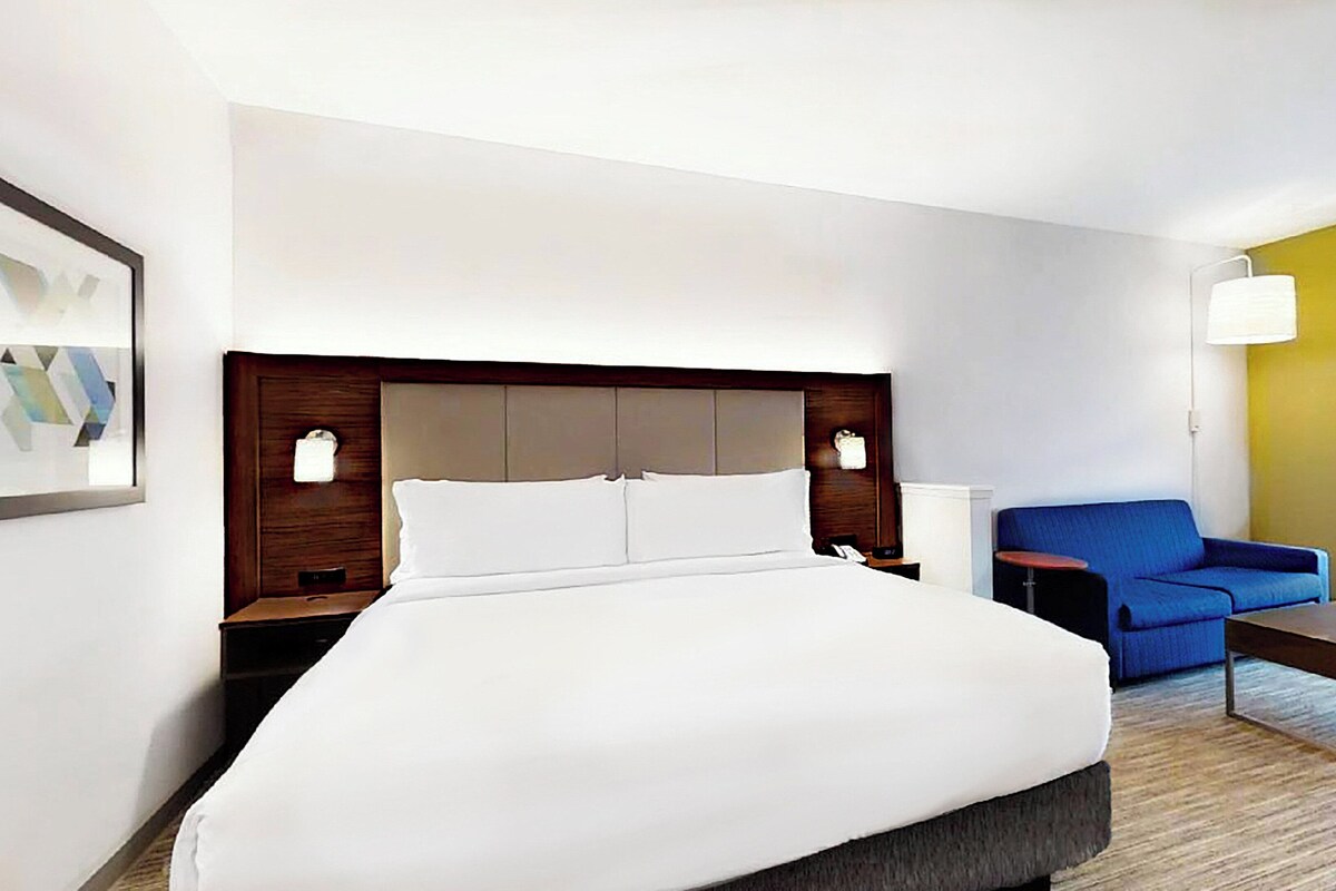 Een hotelkamer met een groot bed, een blauwe fauteuil, een tafeltje en een lamp.
