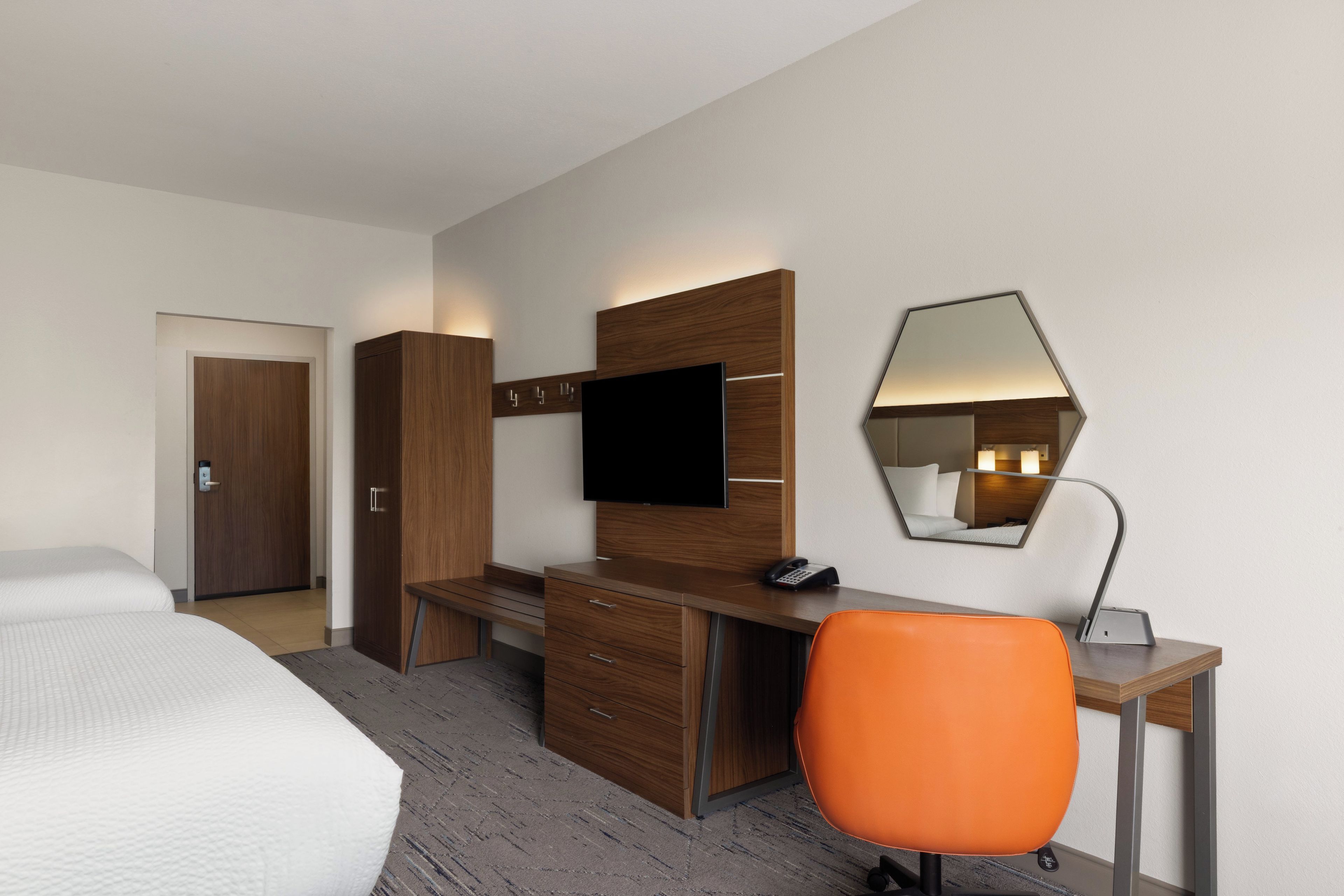 Een hotelkamer met een bed, een bureau met stoel, een televisie, een spiegel en een deur.
