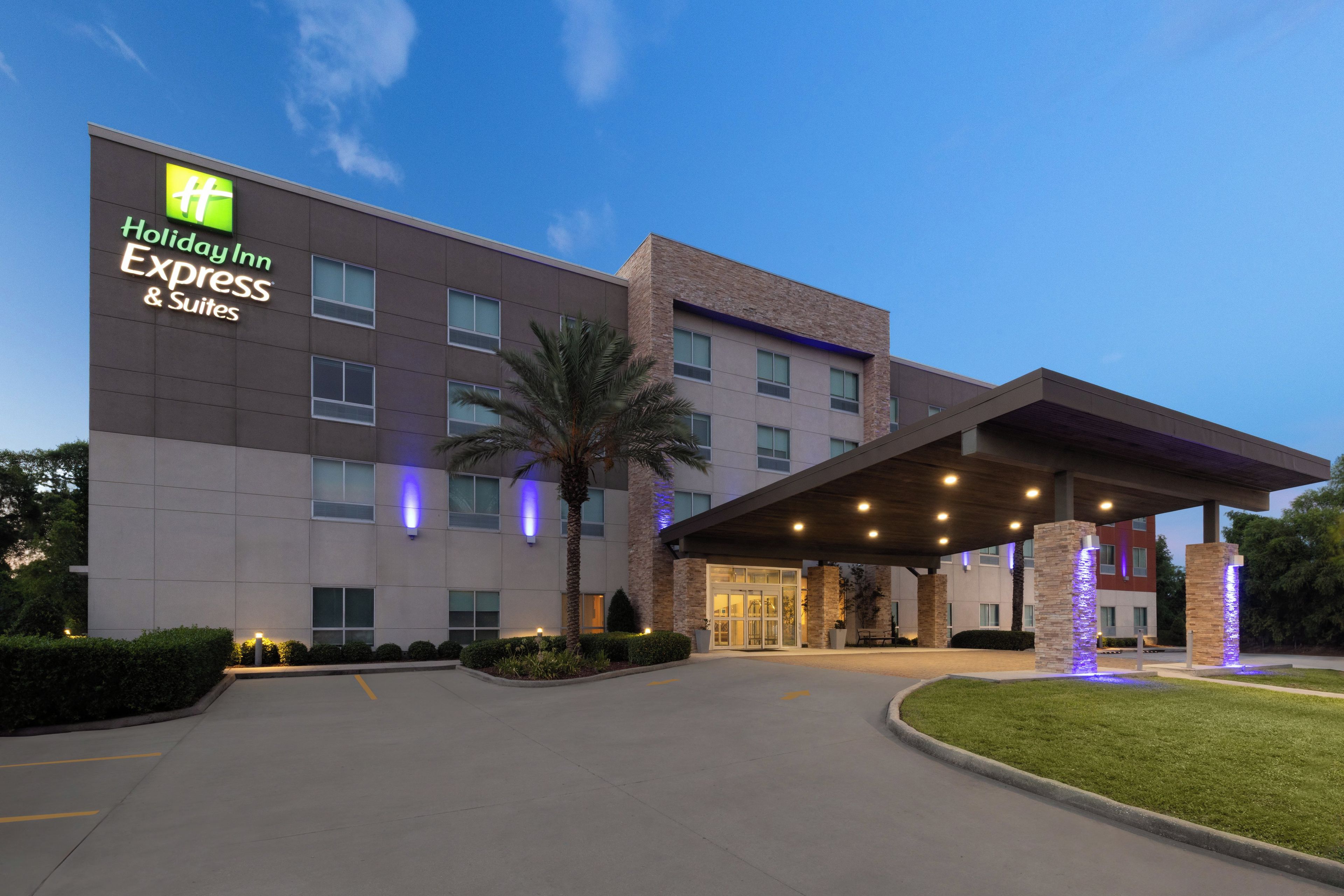 A Holiday Inn Express & Suites building with a modern design, featuring a covered entrance and a well-maintained lawn.