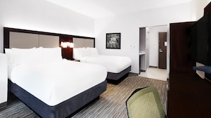 Une chambre d’hôtel avec deux lits, un bureau, une chaise, une télévision et une porte donnant sur une salle de bain.