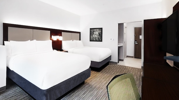 Quarto de hotel com duas camas, uma escrivaninha, uma cadeira, uma televisão e uma porta para o banheiro.