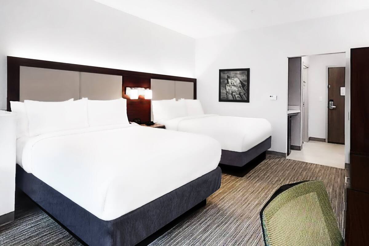 Een hotelkamer met twee bedden, een bureau, een stoel, een televisie en een deur naar een badkamer.