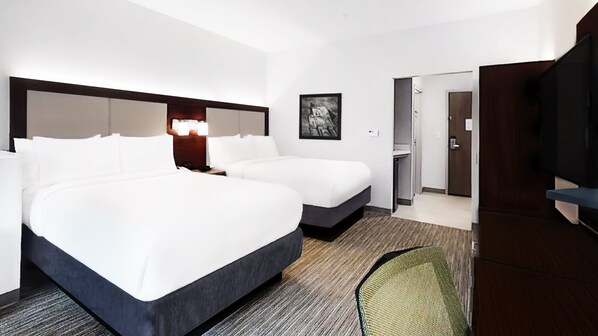 Een hotelkamer met twee bedden, een bureau, een stoel, een televisie en een deur naar een badkamer.