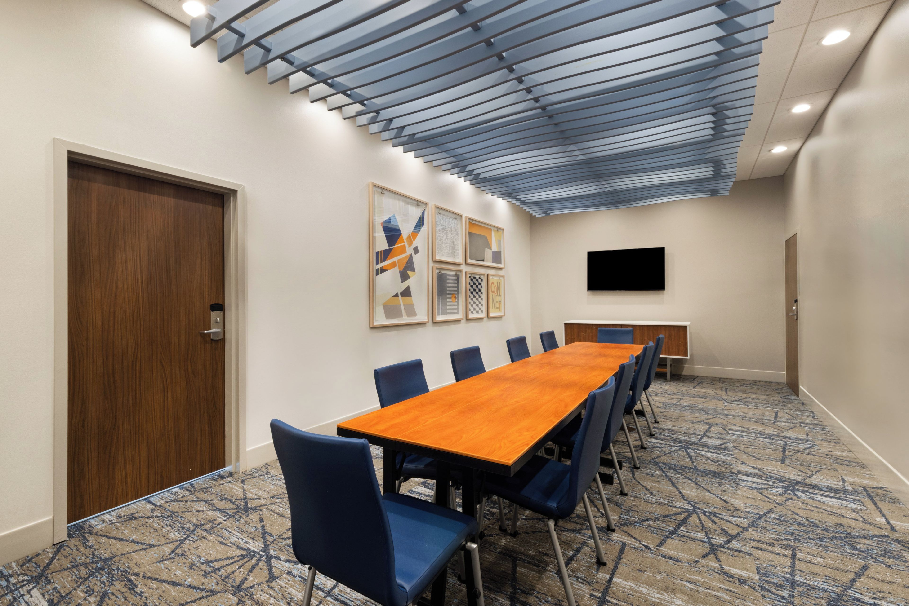 A conference room with a long table, blue chairs, a wooden door, and framed artwork on the wall.
