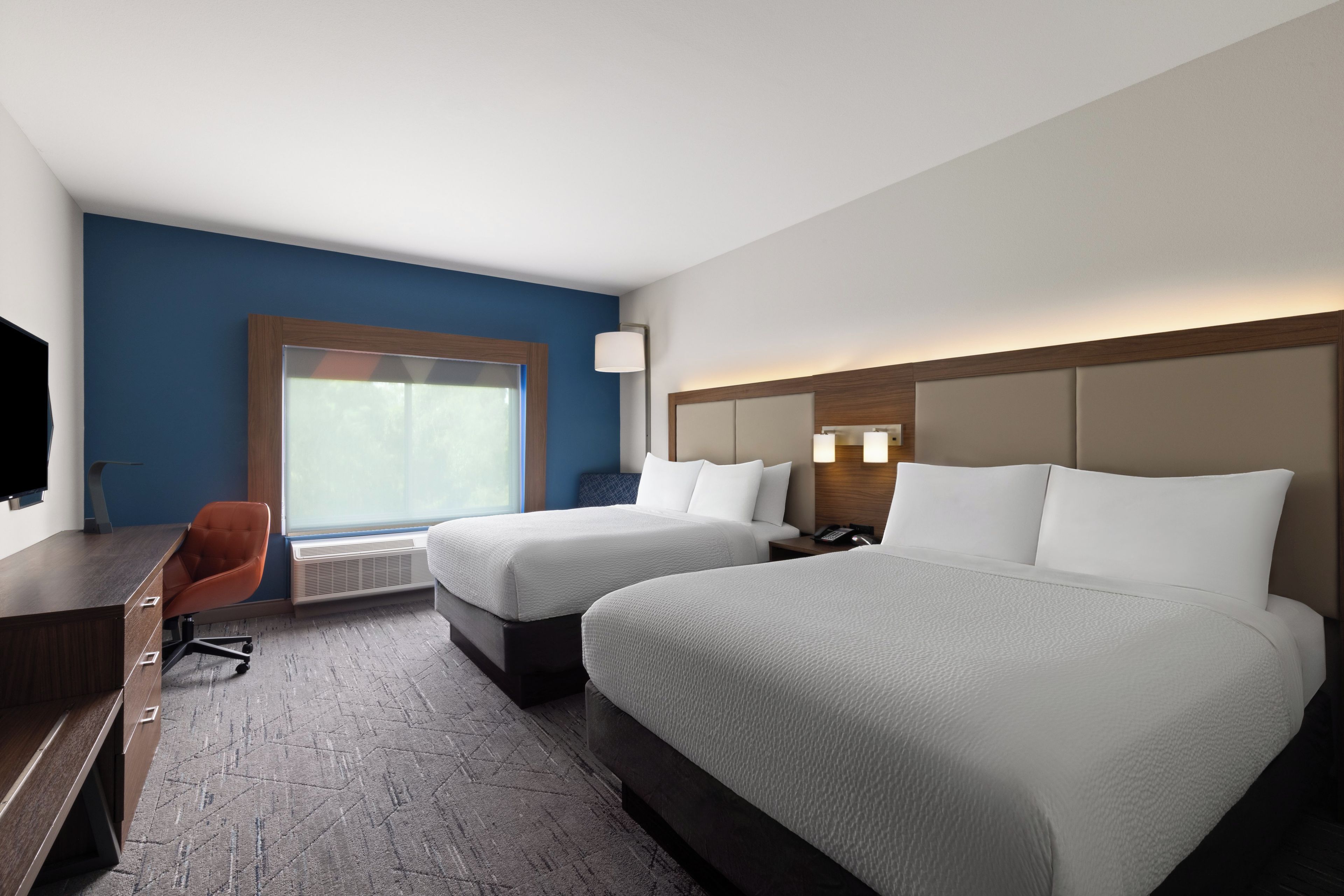 Ein Hotelzimmer mit zwei Betten, einem Schreibtisch, einem Stuhl, einem Fernseher und einem Fenster.