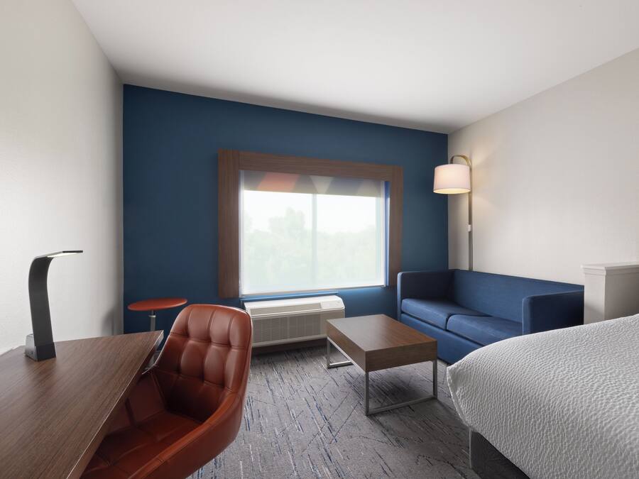 Une chambre d’hôtel comprenant un lit, un canapé, un bureau, une chaise, une table, une lampe et une fenêtre avec des stores.