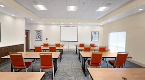 Een vergaderzaal met een projectiescherm, tafels en stoelen klaar voor vergaderingen.