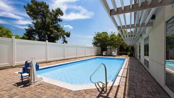A rectangular swimming pool with a white deck surrounding it, a metal pool ladder, and a white fence enclosing the area.