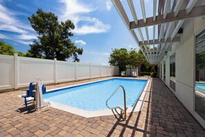 Une piscine rectangulaire entourée d’une terrasse blanche, avec un escalier métallique pour y accéder et une clôture blanche délimitant l’espace.