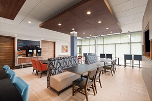 A modern indoor space with seating arrangements, a coffee station, and large windows allowing natural light.