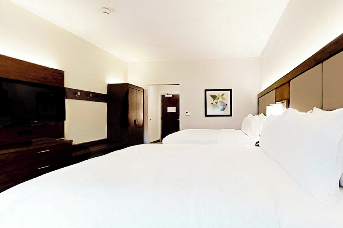 Een hotelkamer met een groot bed, een televisie, een kledingkast en een ingelijst schilderij aan de muur.