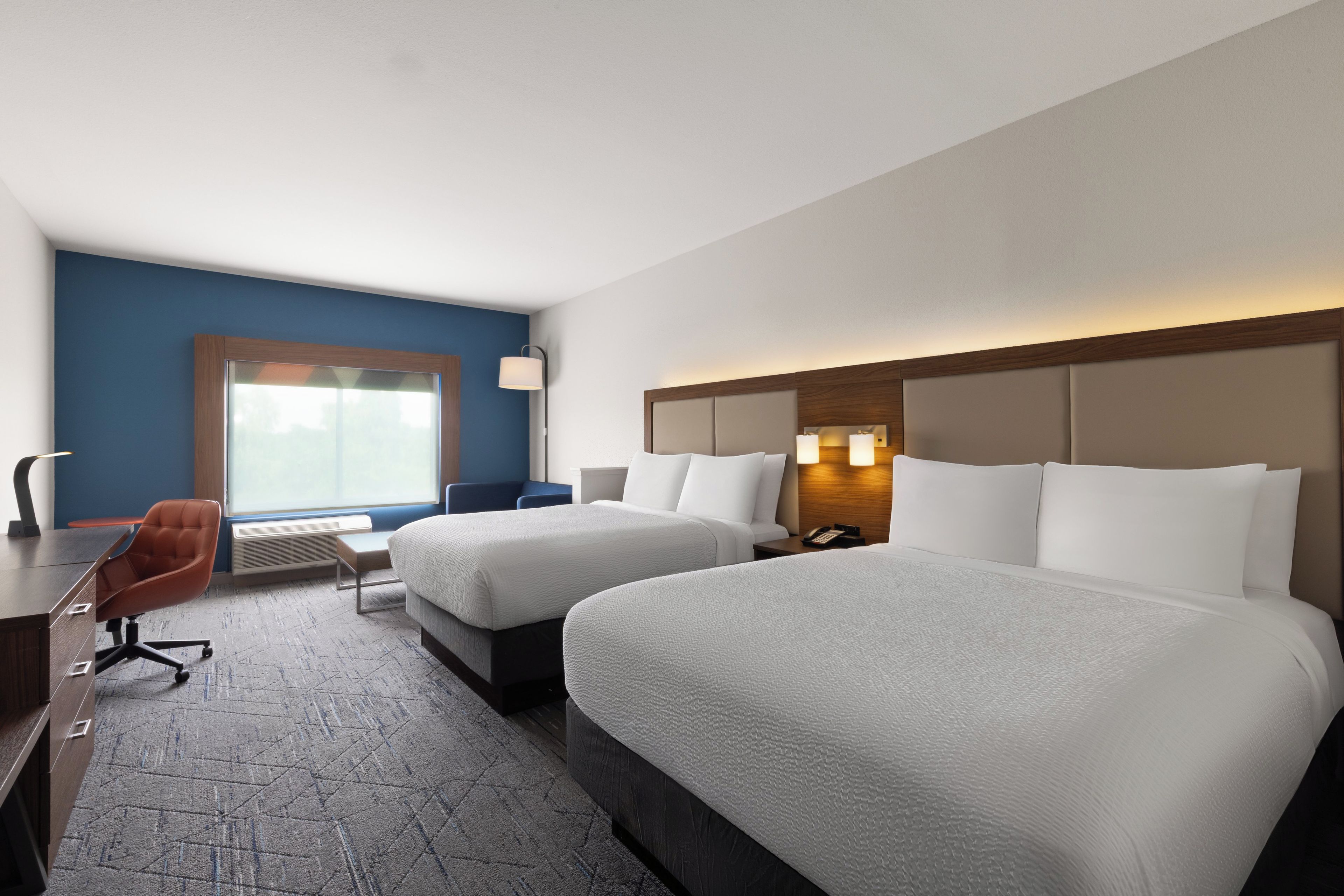 Quarto de hotel com duas camas, uma escrivaninha, uma cadeira e uma janela.