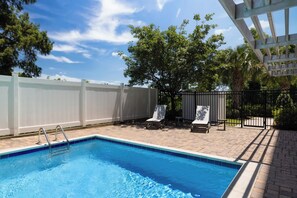 A rectangular swimming pool with a ladder on one side, surrounded by a white fence, and two lounge chairs with a small table. - Holiday Inn Express & Suites Chalmette - New Orleans S by IHG (Chalmette)