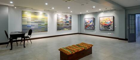 A spacious gallery with modern art on the walls, a wooden bench in the center, and a dining area with chairs and a table.