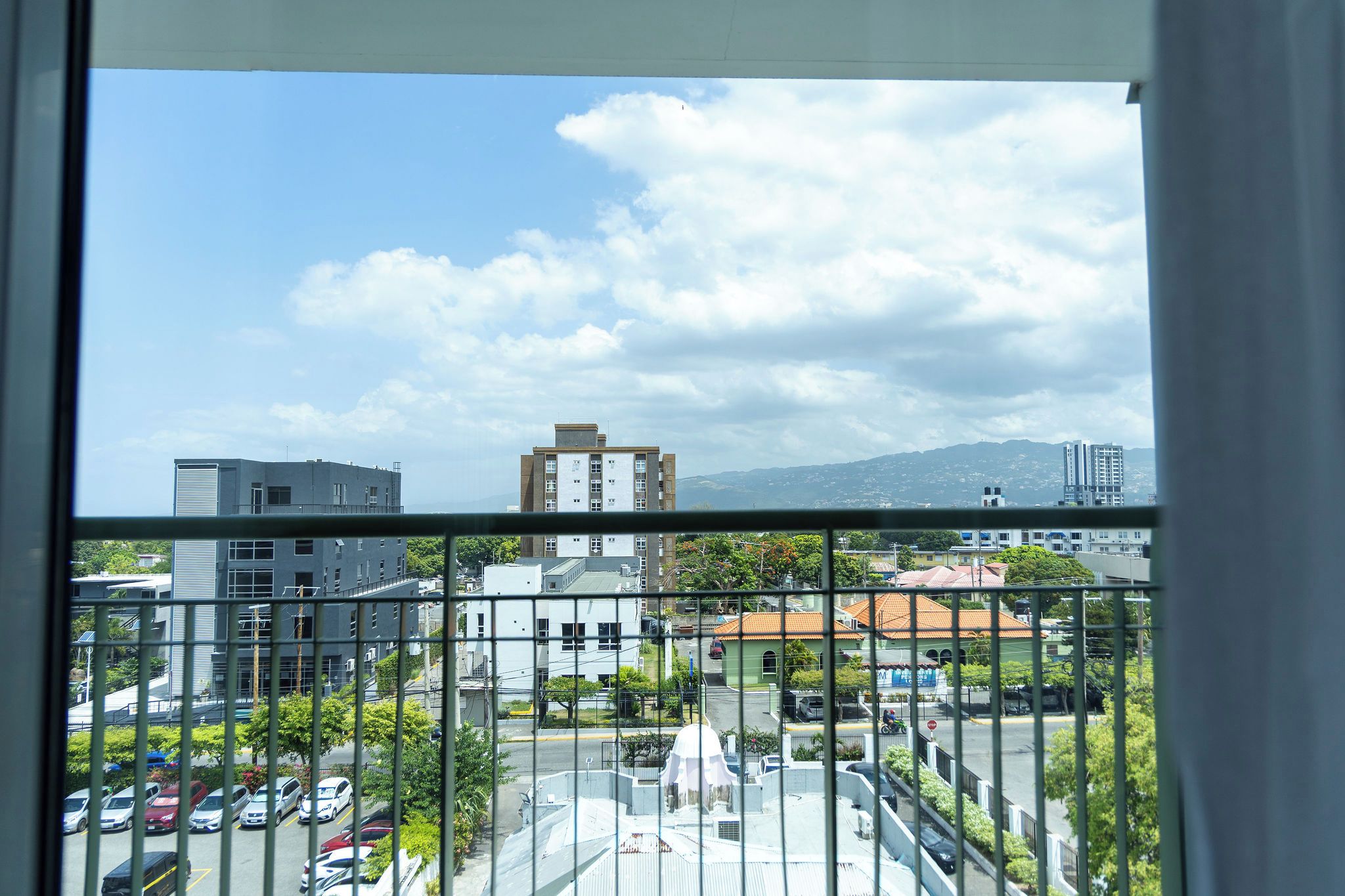 Vista desde una ventana sobre un estacionamiento con edificios y una montaña al fondo.