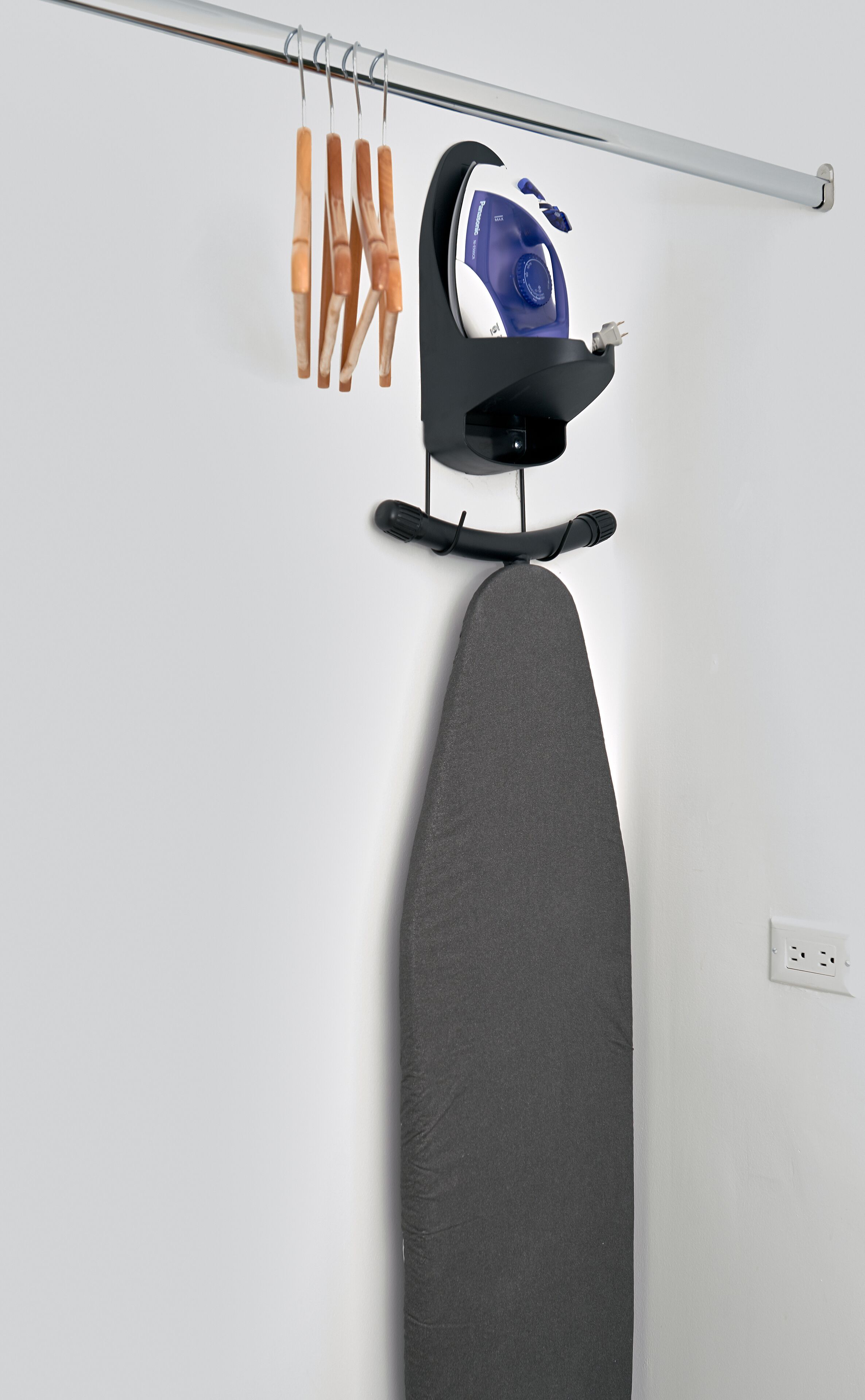 Una tabla de planchar con un plancha y pinzas para la ropa frente a una pared blanca.