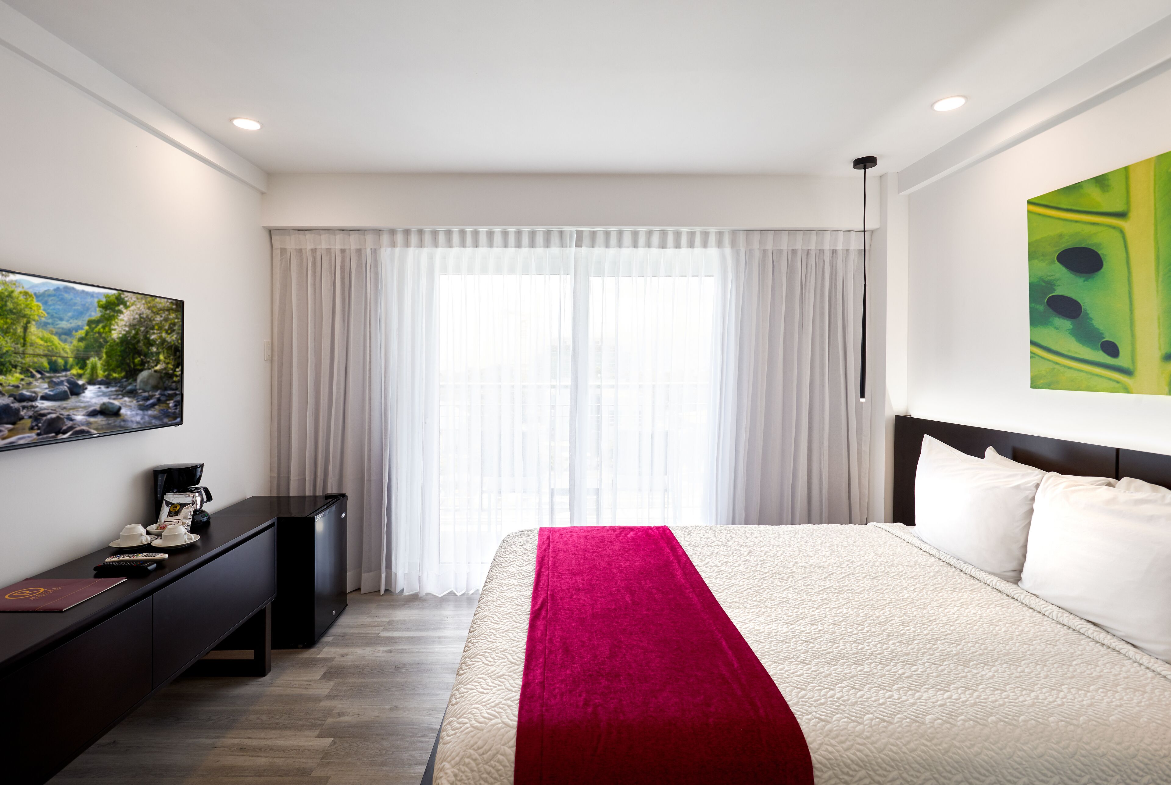 Habitación de hotel con cama, televisión de pantalla plana, escritorio y ventana con cortinas.