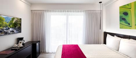 A hotel room with a bed, a flat-screen TV, a desk, and a window with curtains.