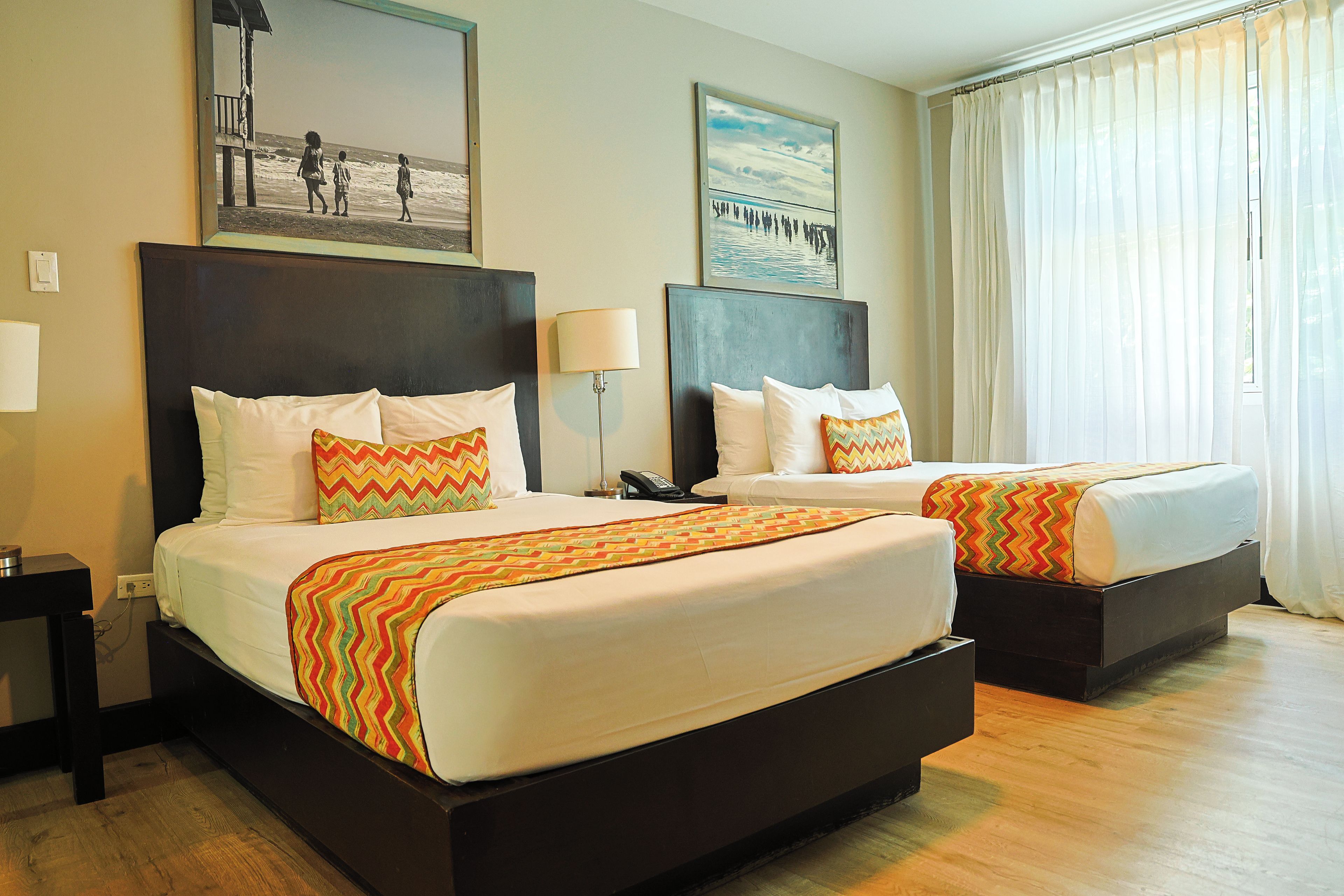 A hotel room with two beds, a nightstand, a lamp, and a painting on the wall.