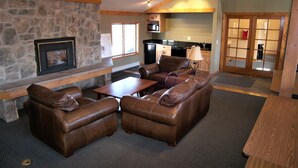 A cozy living room with a stone fireplace, leather sofas, a wooden coffee table, and a kitchen in the background. - Mountainside 2 Bed 2 Bath (Frisco)
