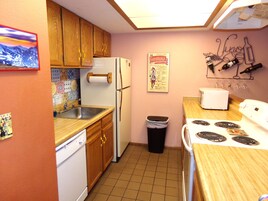Una cocina compacta con armarios de madera, un refrigerador blanco, una estufa y un lavamanos.