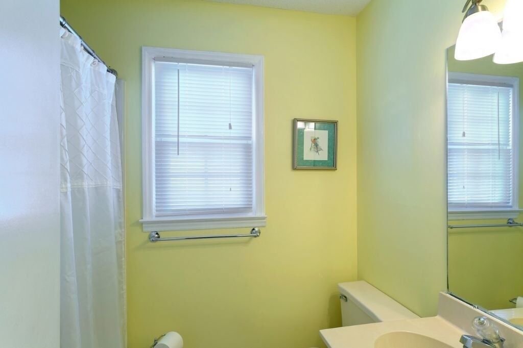 A bathroom with a toilet, sink, and a window with blinds.