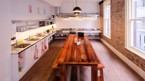 A modern kitchen with a wooden table, stainless steel appliances, and a brick wall. - Haka House Auckland K’ Road (Auckland)