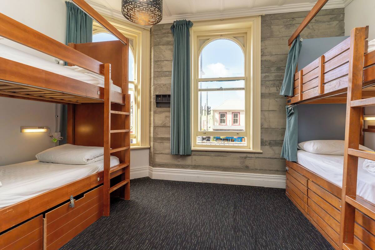 A room with bunk beds, a window with curtains, and a view of a building outside.