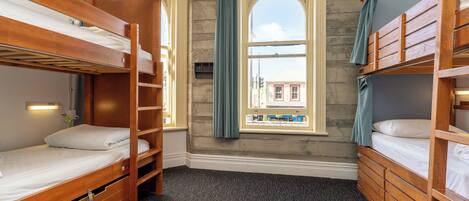 Una habitación con literas, una ventana con cortinas y vista a un edificio.