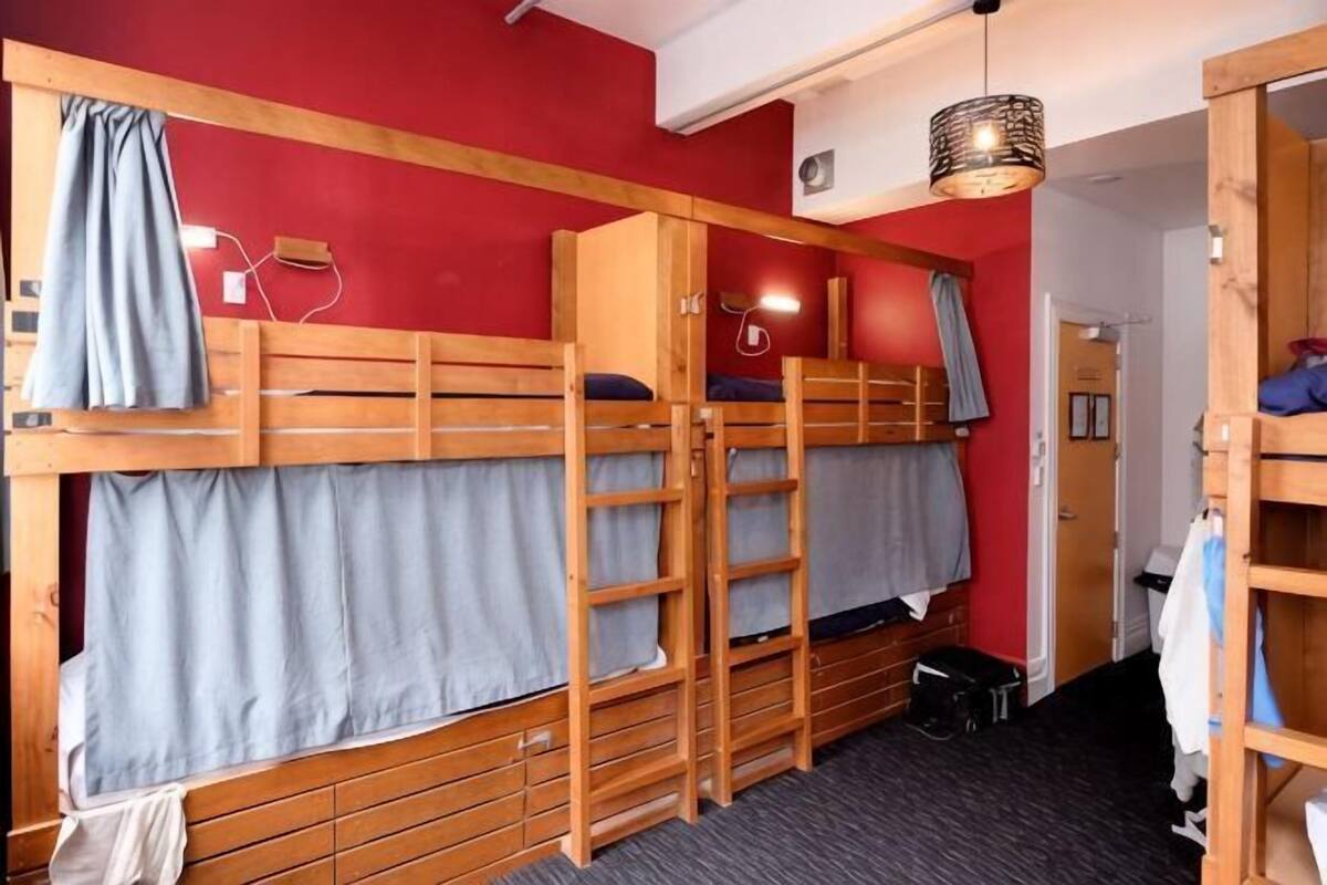 A dormitory room with bunk beds, a wardrobe, a desk, and a hanging light fixture.