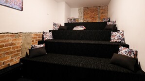 A staircase with black steps and patterned cushions, leading to a seating area with a brick wall and a painting on the wall. - Haka House Auckland K’ Road (Auckland)