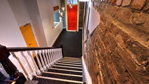 A staircase with a black carpet and white balusters, leading to a red door. - Haka House Auckland K’ Road (Auckland)