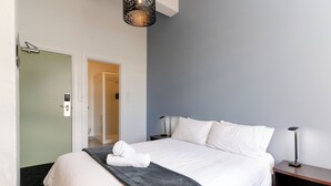 A hotel room with a bed, a bedside table, a lamp, and a door. - Haka House Auckland K’ Road (Auckland)