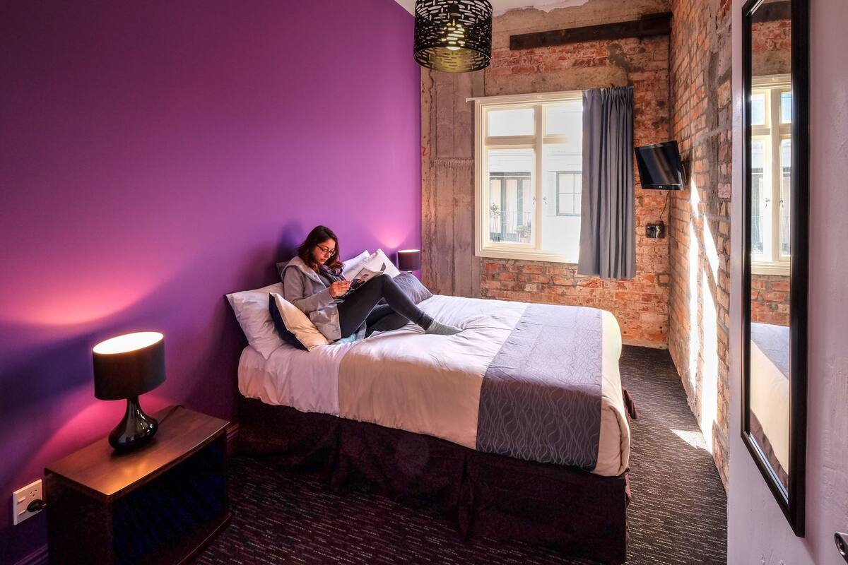 A room with a bed, a lamp, a TV, and a window with curtains.