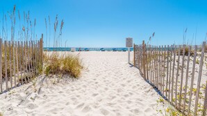 A sandy beach path leading to the ocean with a wooden fence on one side and a signpost in the center.