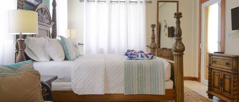 Quarto com cama grande, cabeceira de madeira, janela com cortinas, mesa de cabeceira com abajur e cômoda de madeira.