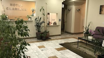 Hall d'albergo con reception, piante in vaso, banco accettazione e area relax con divano.