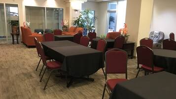 Uma sala de conferências com várias mesas e cadeiras, paredes de vidro e plantas em vasos.
