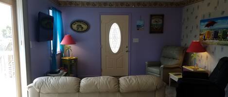 A living room with a beige sofa, a chair, a small table with a lamp, and a door with a window.