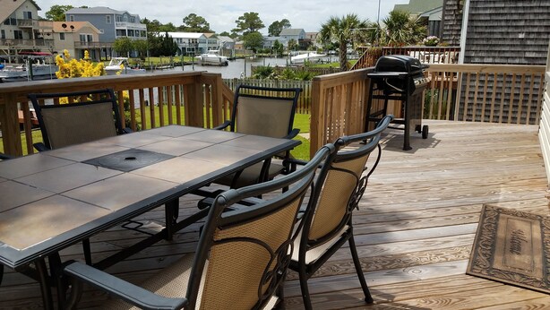 Um deck externo com mesa e cadeiras, com vista para um corpo d'água e um porto de embarcações.